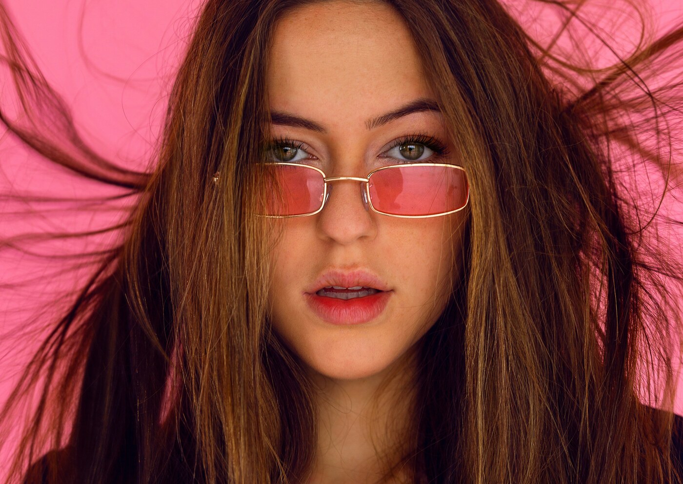 Close-up of a woman wearing rose-tinted rectangular sunglasses
